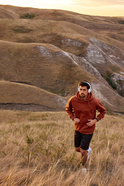 Rear view sports runner man jogging on field among mountains, beautiful landscape - Фото, зображення