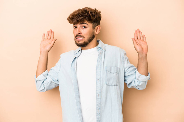 Young arab man isolated on beige background being shocked due to an imminent danger - Foto, immagini
