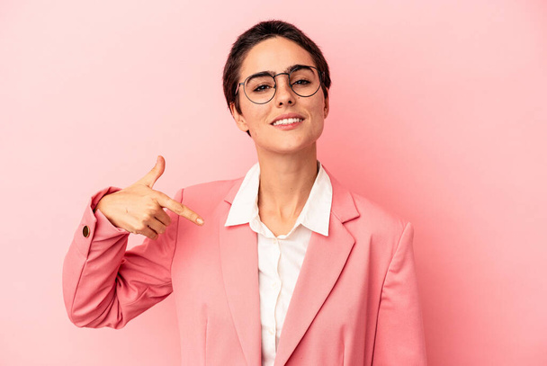 Joven mujer de negocios con una chaqueta rosa aislada sobre fondo rosa persona que señala a mano a un espacio de copia de la camisa, orgulloso y seguro - Foto, imagen