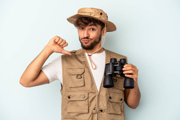 Young mixed race man holding binoculars isolated on blue background feels proud and self confident, example to follow. - Photo, Image
