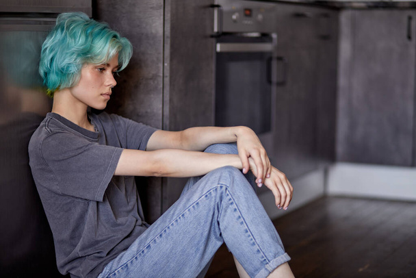 Depressed female upset with something, sitting alone on floor in kitchen - Foto, afbeelding