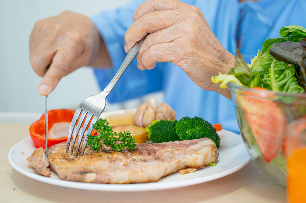Азиатская пожилая женщина пожилого возраста или пожилая женщина пациентка, питающаяся завтраком и овощной здоровой пищей с надеждой и счастливой, сидя и голодный на кровати в больнице. - Фото, изображение