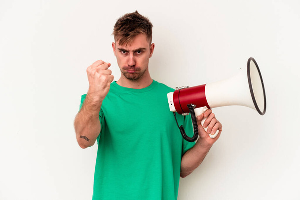 Young caucasian man holding megaphone isolated on white background showing fist to camera, aggressive facial expression. - Photo, Image