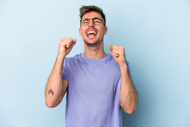 Young caucasian man isolated on blue background celebrating a victory, passion and enthusiasm, happy expression. - Fotoğraf, Görsel
