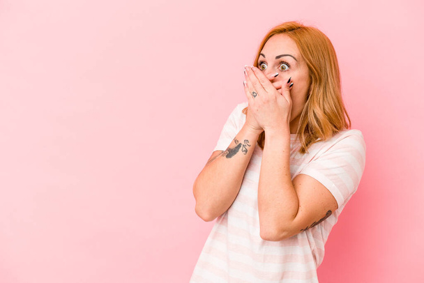 Νεαρή καυκάσια γυναίκα απομονωμένη σε ροζ φόντο στοχαστική ψάχνει σε ένα χώρο αντίγραφο που καλύπτει το στόμα με το χέρι. - Φωτογραφία, εικόνα