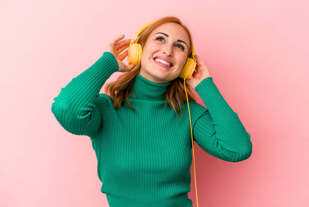 Молодая белая женщина слушает музыку на розовом фоне - Фото, изображение