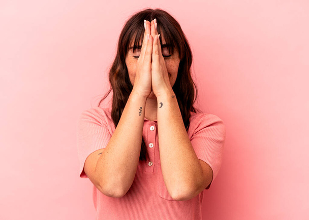 Fiatal argentin nő elszigetelt rózsaszín háttér fogja kezét imádkozni közel száj, úgy érzi, magabiztos. - Fotó, kép