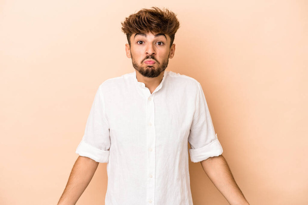 Young arab man isolated on beige background shrugs shoulders and open eyes confused. - Фото, зображення