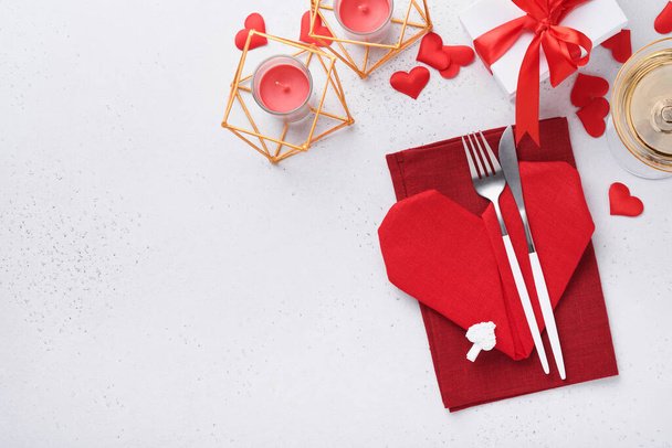 Valentinas day table setting white color with white silverware, red napkin folded as heart, candles, champagne, glasses on white background for greetings. Romantic dinner or menu concept. Mock up. - Foto, afbeelding