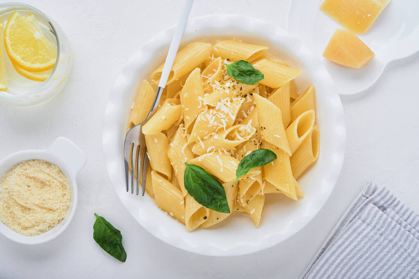 Tasty appetizing classic italian penne pasta with parmesan cheese and basil in white plate on plate on on stone table. Traditional dish of Italian cuisine. Top view. - Фото, зображення