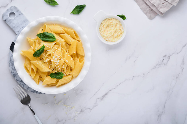 Tasty appetizing classic italian penne pasta with parmesan cheese and basil in white plate on plate on on stone table. Traditional dish of Italian cuisine. Top view. - Φωτογραφία, εικόνα