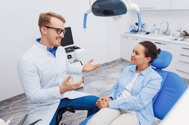 Smiling male dentist explaining client about dental procedure in clinic with modern equipment - Фото, изображение