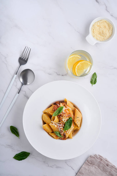 Bolognese Penne Pasta. Tasty appetizing classic italian penne pasta with parmesan cheese, basil and Bolognese sauce in white plate on plate on stone table Traditional dish of Italian cuisine. Top view - Fotoğraf, Görsel