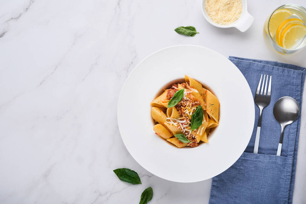 Bolognese Penne Pasta. Tasty appetizing classic italian penne pasta with parmesan cheese, basil and Bolognese sauce in white plate on plate on stone table Traditional dish of Italian cuisine. Top view - Photo, image