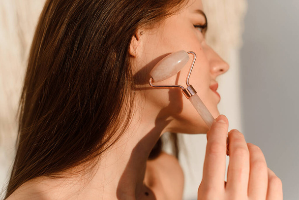 Young woman with fresh radiant skin doing a spa facial at home. Natural Jade Face Lift Roller, Rejuvenating Facial Massage - Foto, Imagem