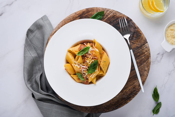 Bolognese Penne Pasta. Tasty appetizing classic italian penne pasta with parmesan cheese, basil and Bolognese sauce in white plate on plate on stone table Traditional dish of Italian cuisine. Top view - Foto, Bild