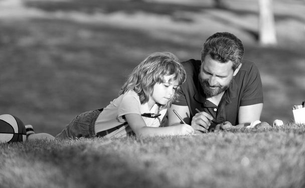 padre e hijo relajarse en la hierba en el parque aprendiendo a dibujar, paternidad - Foto, imagen