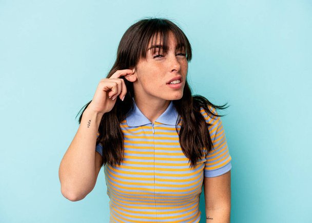 Junge Argentinierin isoliert auf blauem Hintergrund, die Ohren mit Fingern bedeckt, gestresst und verzweifelt durch eine laute Umgebung. - Foto, Bild