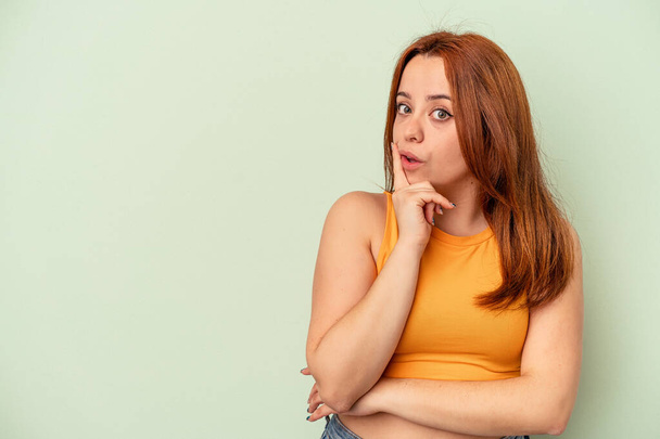 Young caucasian woman isolated on green background looking sideways with doubtful and skeptical expression. - Photo, Image