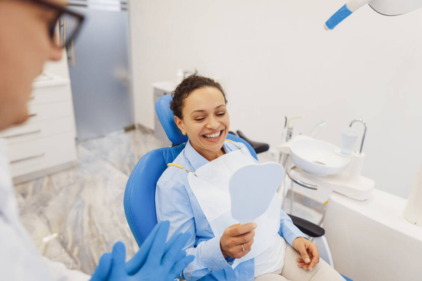 Overhead view of client sitting in dental chair and looking in the mirror on teeth after dental procedure - Foto, afbeelding