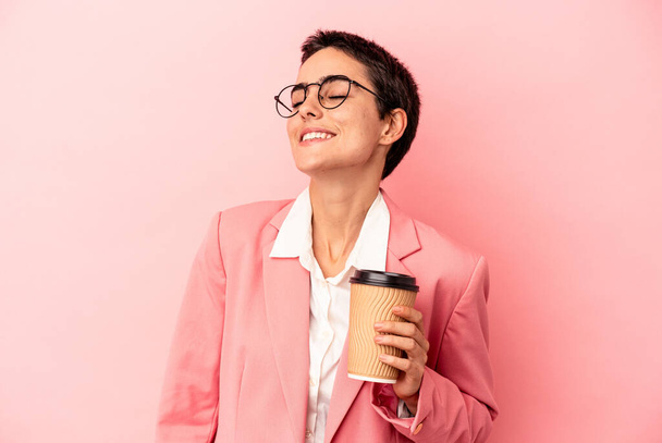 Junge kaukasische Geschäftsfrau hält einen Kaffee zum Mitnehmen auf rosa Hintergrund und träumt davon, Ziele und Zwecke zu erreichen - Foto, Bild