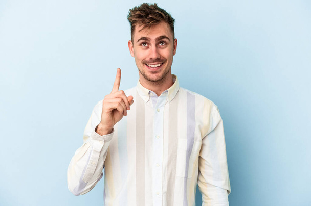 Young caucasian man isolated on blue background indicates with both fore fingers up showing a blank space. - Photo, Image