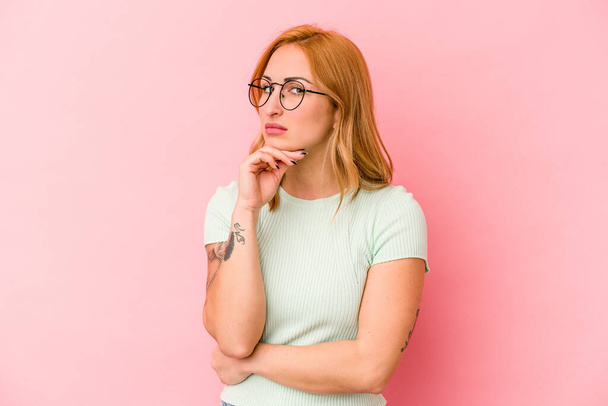 Young caucasian woman isolated on pink background suspicious, uncertain, examining you. - Photo, Image