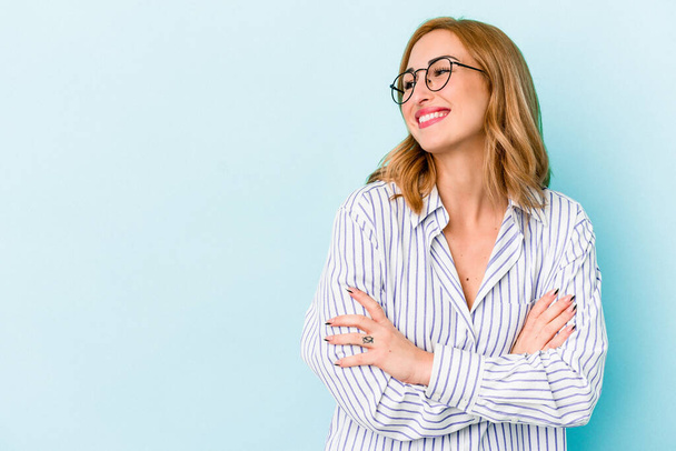 Young caucasian woman isolated on blue background smiling confident with crossed arms. - Photo, Image