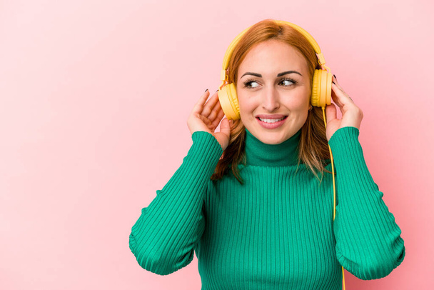 Young caucasian woman listening to music isolated on pink background - Фото, зображення