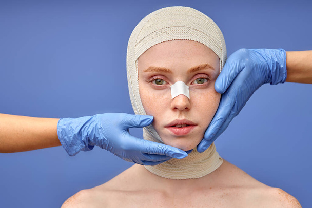 cropped surgeon in gloves taping up woman face with bandage after plastic surgery - Foto, immagini