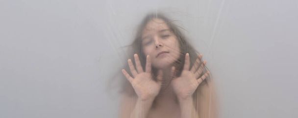 Wazig, onscherp portret van mooie sexy sensuele verleidelijke lockdown sensuele tevreden vrouw achter plastic folie in nachtmerrie droom, heft defensieve handen voor bescherming, kopieer ruimte - Foto, afbeelding