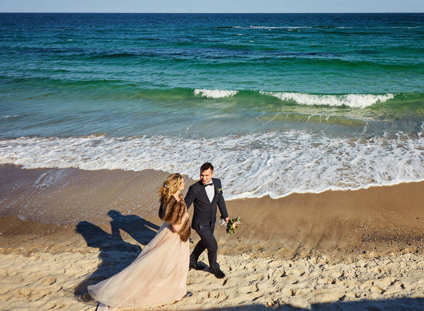 Happy young newly married couple woman in white dress man in love running, have fun on clean sandy beach waves of azure sea or ocean, summer vacation at water. Wedding rest, relax honeymoon concept. - Photo, Image