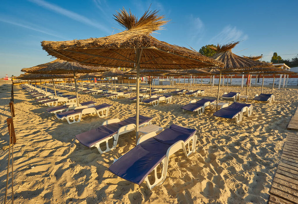 Соломенные пляжные зонтики и шезлонги на пляже на идиллическом тропическом курорте для летнего отдыха - Фото, изображение