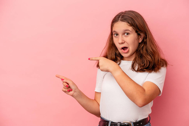 Kleines kaukasisches Mädchen, isoliert auf rosa Hintergrund, zeigt mit den Zeigefingern auf einen Kopierraum und drückt damit Begeisterung und Wunsch aus. - Foto, Bild