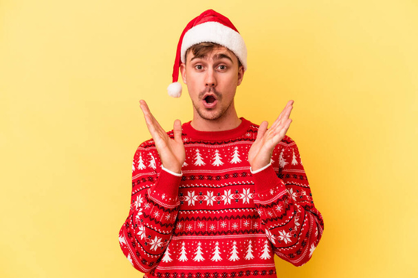 Young caucasian man celebrating Christmas isolated on yellow background surprised and shocked. - Foto, Imagem