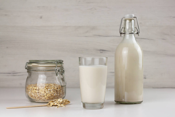 Dairy free oat milk and flakes in a glass jar on light background - Zdjęcie, obraz