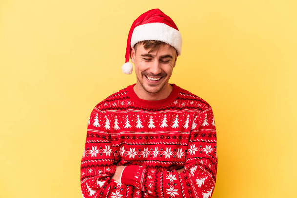 Genç beyaz adam Noel 'i kutluyor. Sarı arka planda izole edilmiş. Gülüyor ve eğleniyor.. - Fotoğraf, Görsel