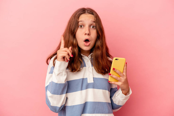 Little caucasian girl holding mobile phone isolated on pink background having an idea, inspiration concept. - Фото, зображення
