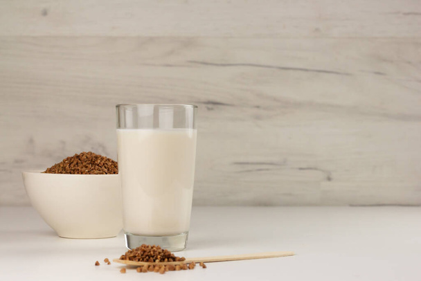 Dairy free buckwheat milk in a glass and buckwheat grains in a bowl - Foto, afbeelding