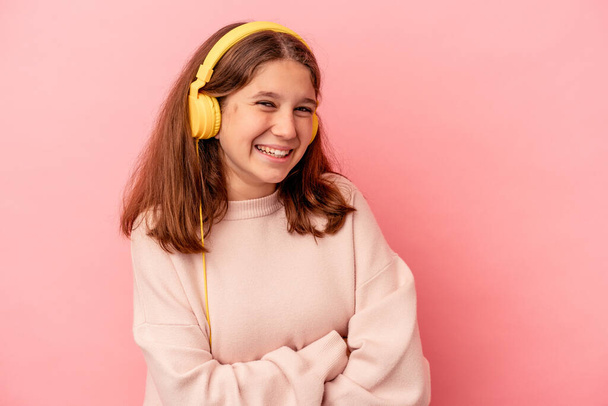 Little caucasian girl listening to music isolated on pink background laughing and having fun. - Фото, изображение