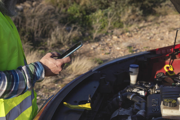 Hombre adulto sosteniendo su capó del coche abierto y enviando mensajes de texto a un mecánico porque su coche se rompió en medio de la carretera - Foto, Imagen