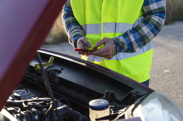 Homem adulto segurando seu capuz de carro aberto e mensagens de texto de um mecânico porque seu carro quebrou no meio da estrada - Foto, Imagem