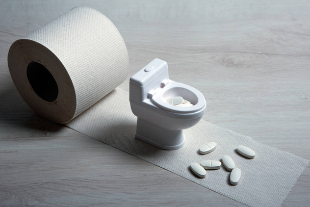 Toilettenschüssel Miniatur und Pillen mit Toilettenpapierrolle auf dem Tisch Nahaufnahme - Foto, Bild