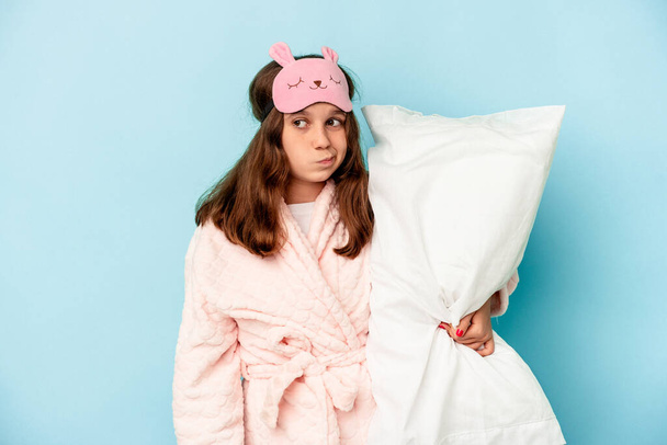 Little caucasian girl going to sleep isolated on blue background confused, feels doubtful and unsure. - Fotoğraf, Görsel