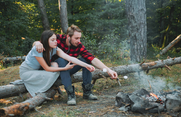 Summer lifestyle. Couple in love having hike picnic nature background. Funny couple eating roasted marshmallows while camping near the lake. Couple in love enjoying picnic in the forest. - Zdjęcie, obraz
