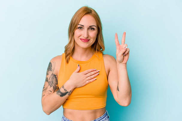 Young caucasian woman isolated on blue background taking an oath, putting hand on chest. - Photo, Image