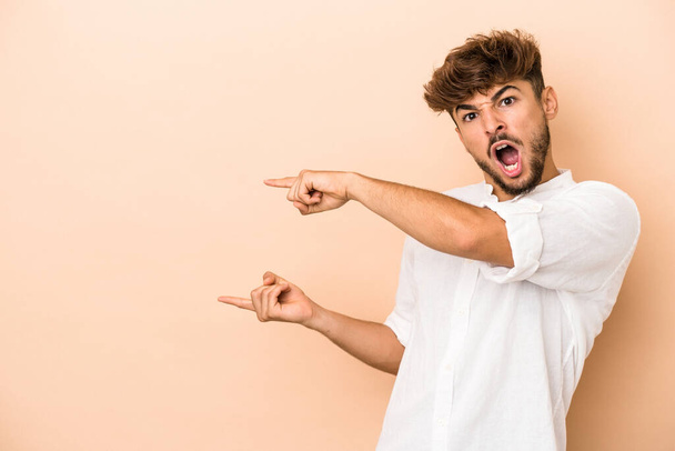 Young arab man isolated on beige background excited pointing with forefingers away. - Fotografie, Obrázek