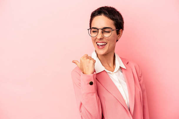 Joven mujer de negocios con una chaqueta rosa aislada en puntos de fondo rosa con el dedo pulgar lejos, riendo y sin preocupaciones. - Foto, imagen