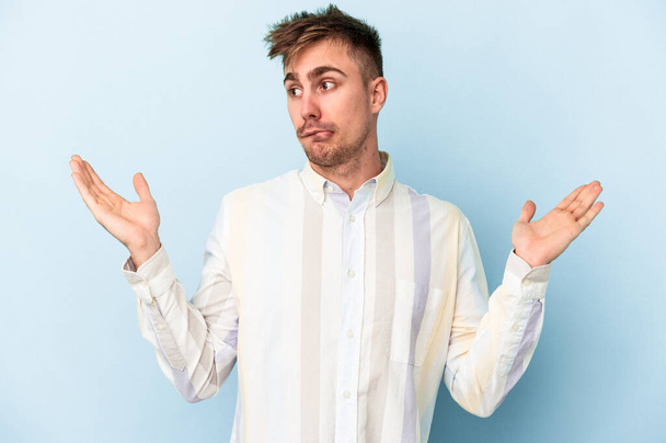 Young caucasian man isolated on blue background confused and doubtful shrugging shoulders to hold a copy space. - Photo, Image