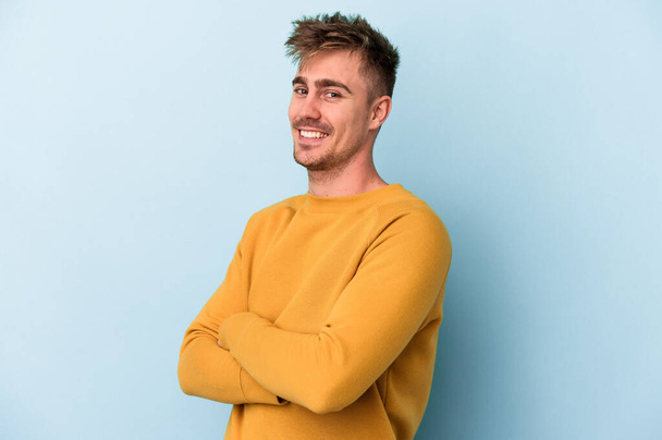 Young caucasian man isolated on blue background happy, smiling and cheerful. - Photo, Image
